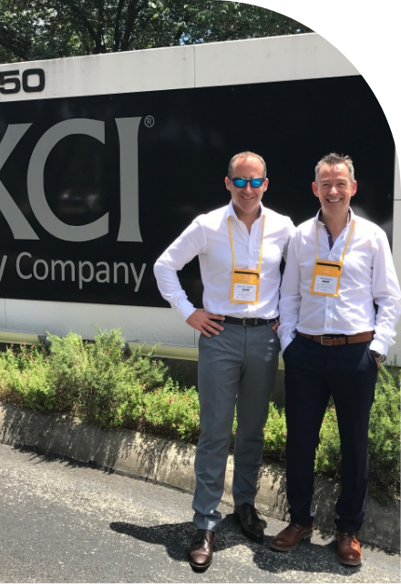 Two men standing in front of the kci company sign advertising custom label solutions.