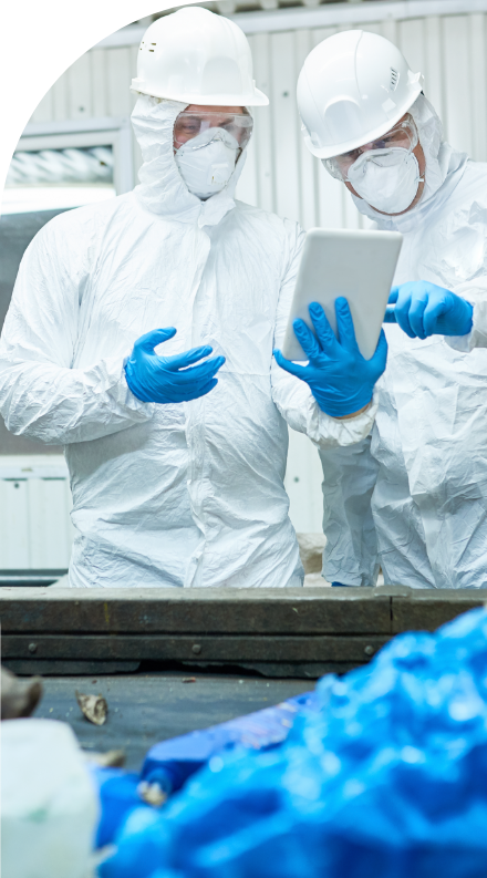 Two workers in protective suits looking at a tablet with high quality labels.