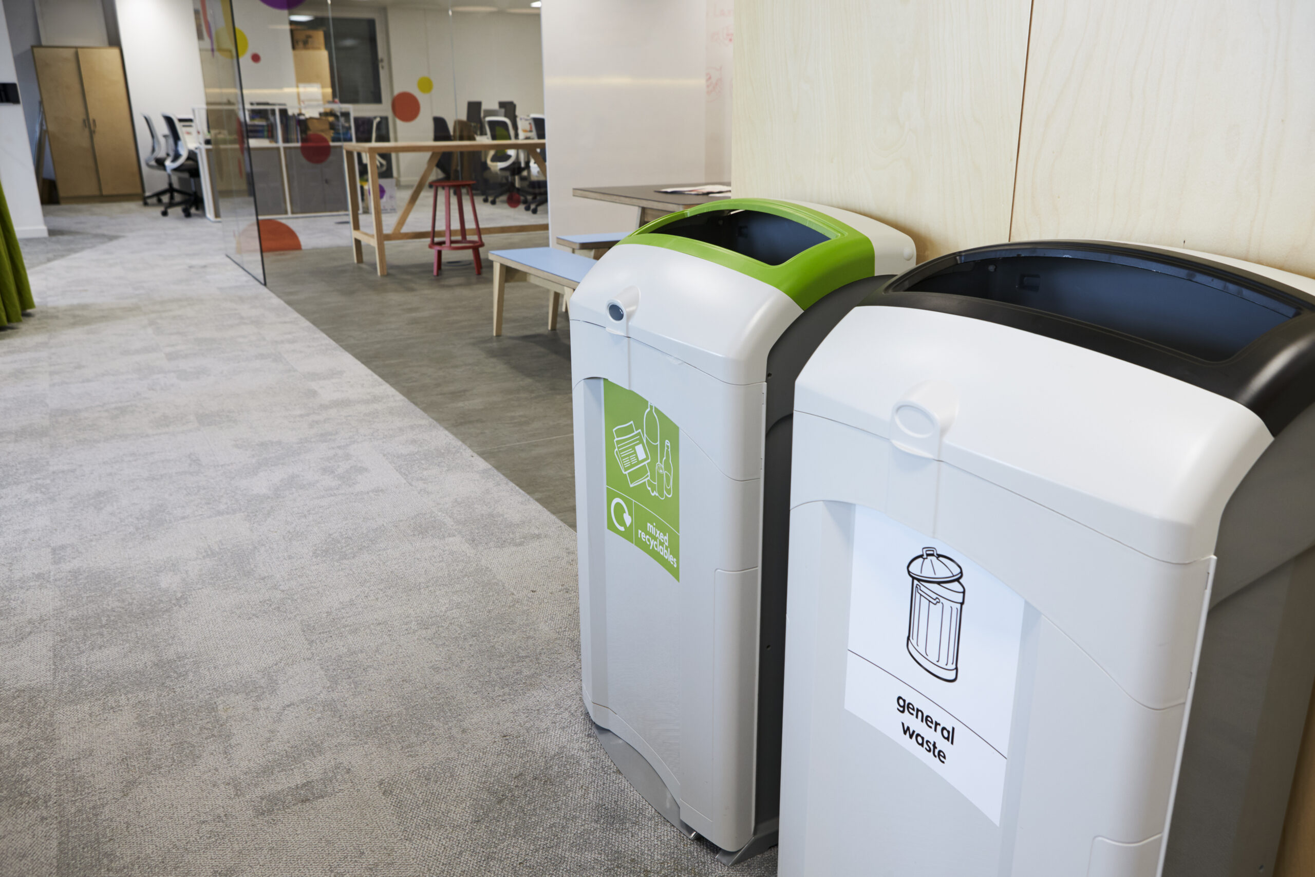 Two customized green and white trash cans in an office with custom label solutions.