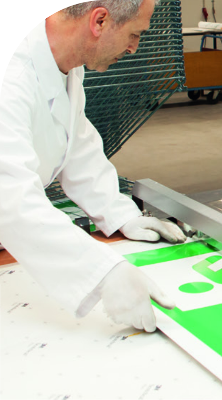 A man in a white coat working on a high quality green sign.