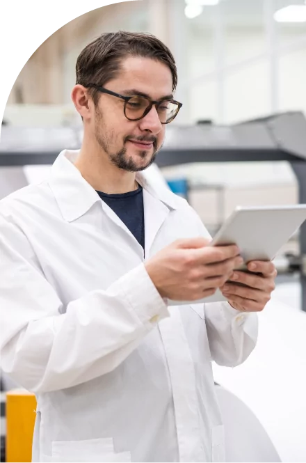 A man in a lab coat using a tablet to create high quality medical labels in a factory.