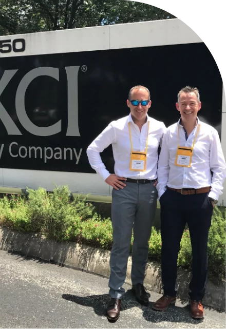 Two men standing in front of the kci company sign advertising custom label solutions.